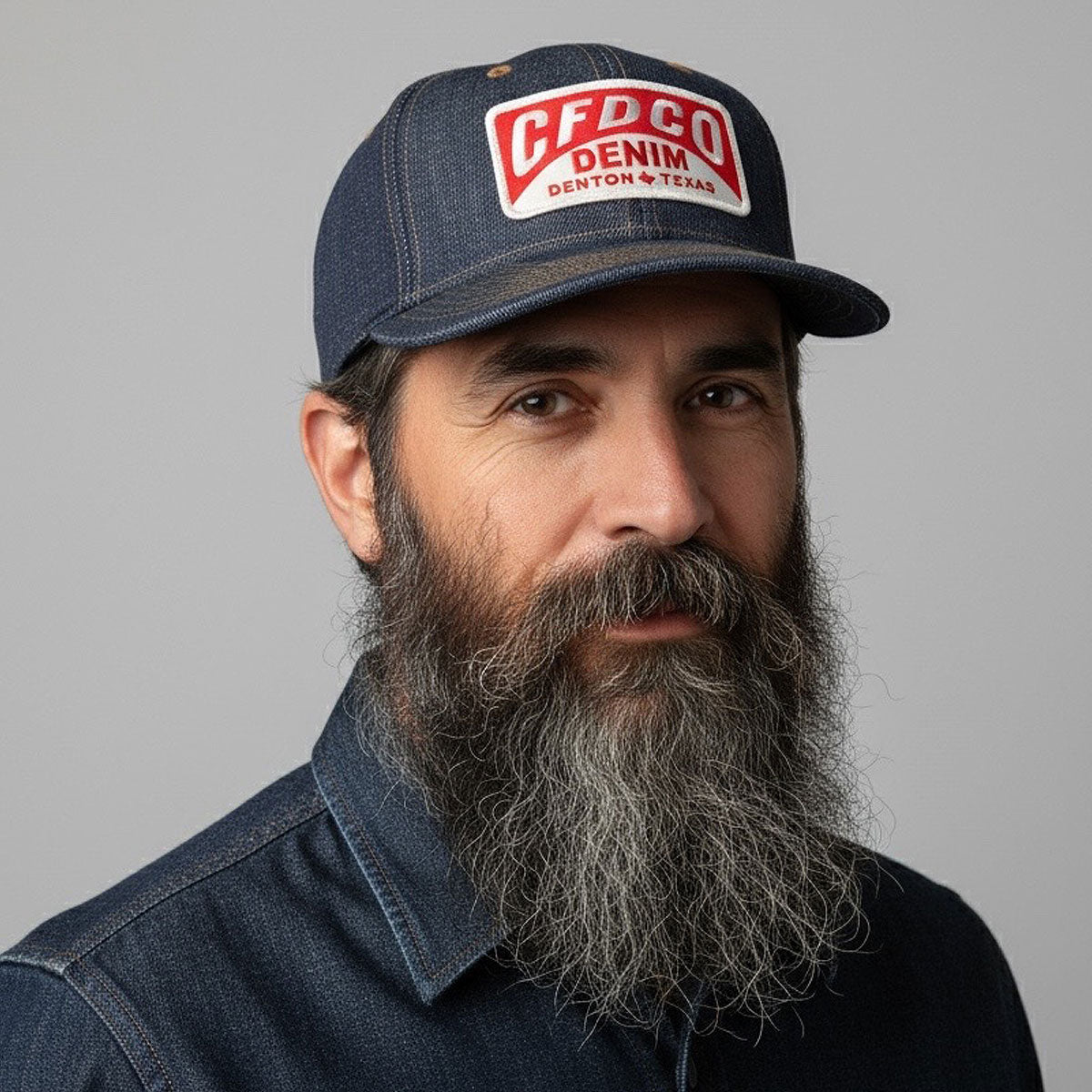 Man wearing a denim cap with a visible brand logo on a gray background