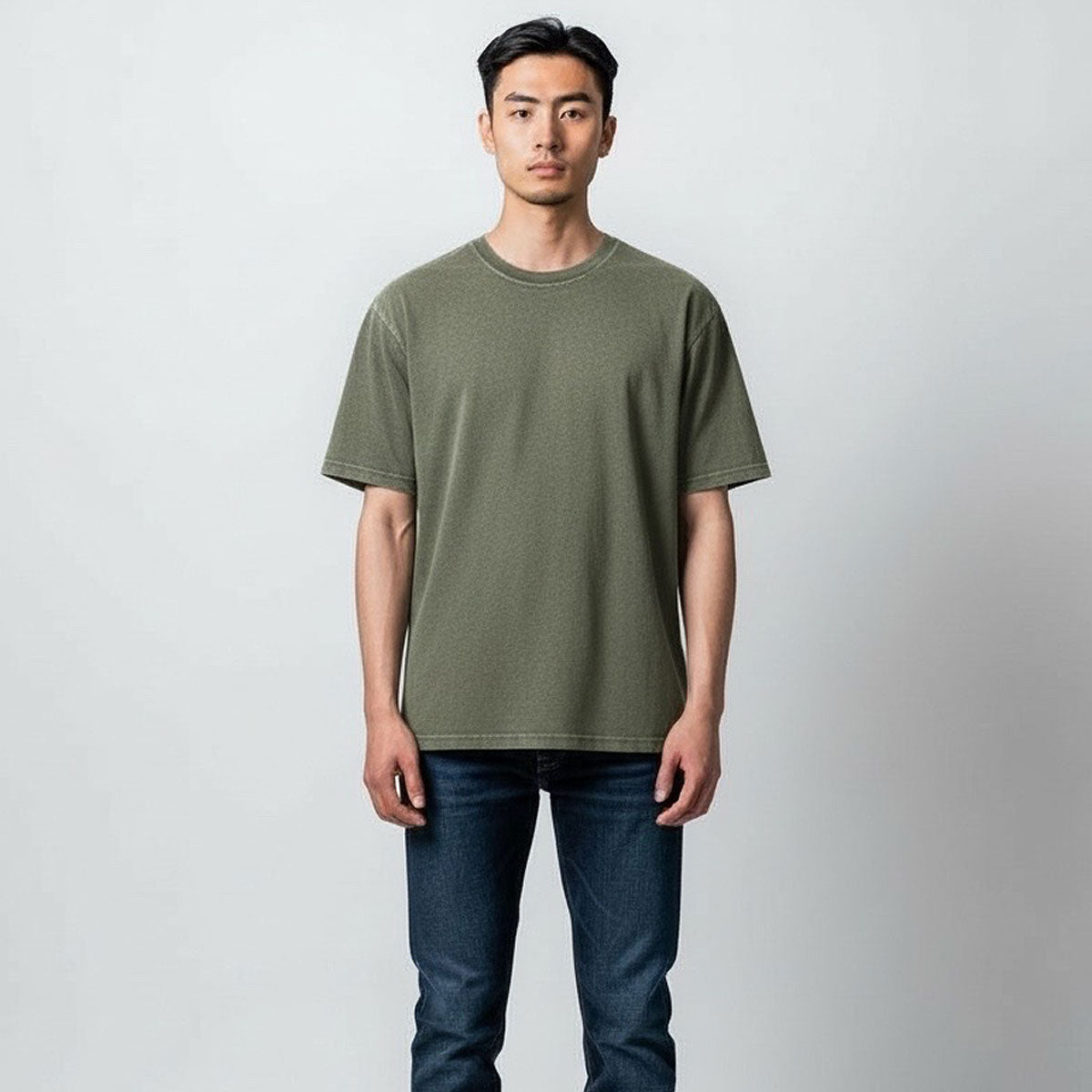 Man wearing an olive green t-shirt and blue jeans against a plain background