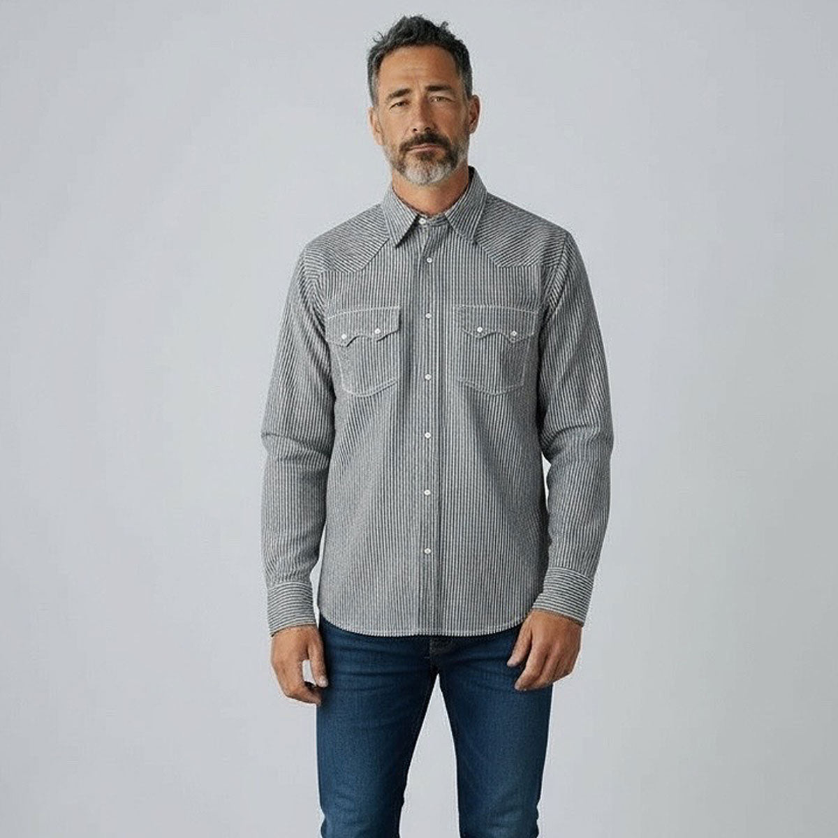 Man wearing a hickory shirt and blue jeans against a plain background