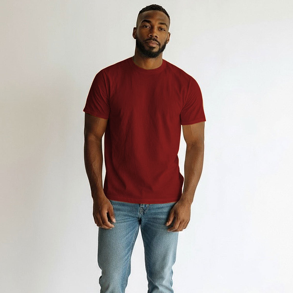 Man wearing a red t-shirt and blue jeans against a plain background
